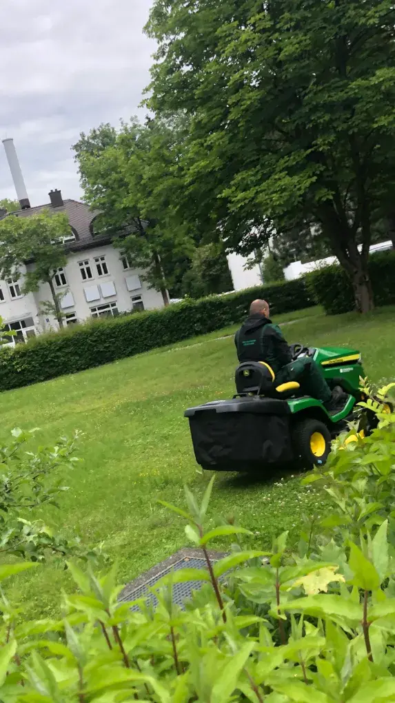 Mitarbeiter mäht mit dem Aufsitzmäher eine große Grünfläche